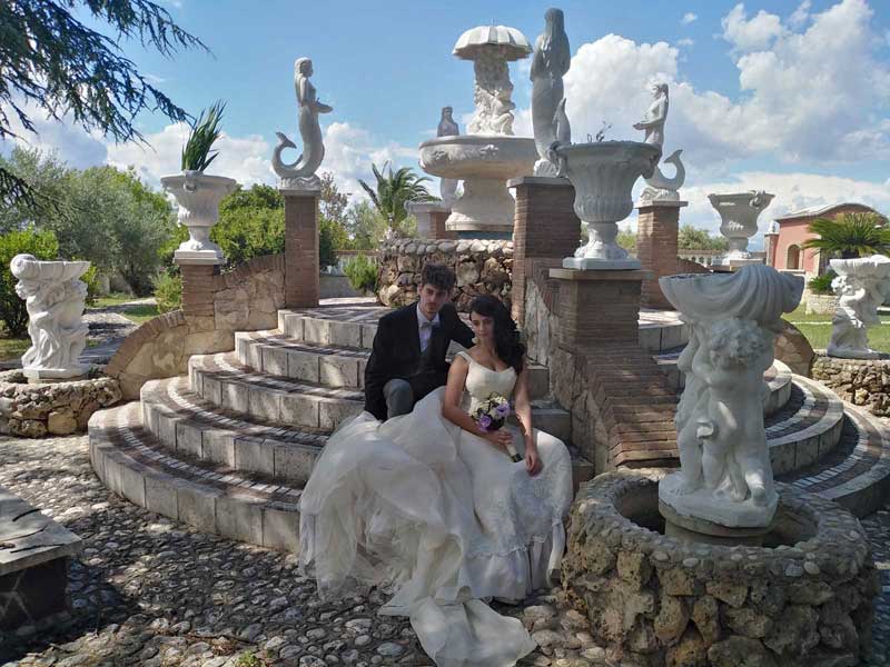 Modelli sposi seduti a bordo fontana - Fotografie abiti cerimonia ricevimento moda uomo donna. Shooting fotografico vestiti sposa location Villa Fravili
